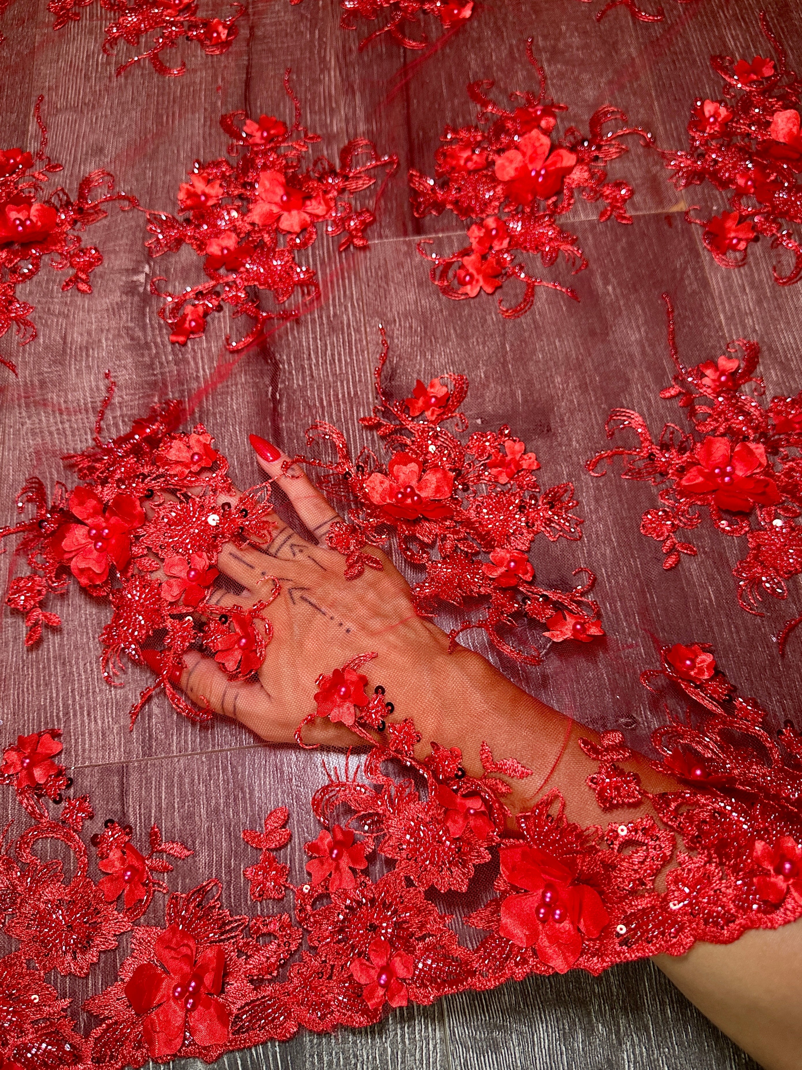 Red floral lace fabric with a hand touching it on a dark background