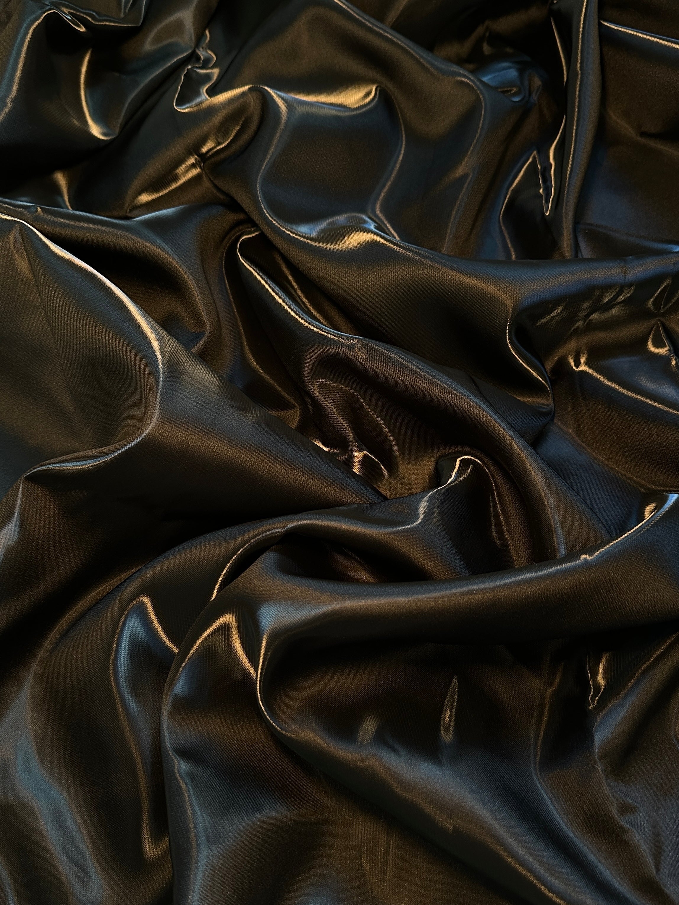 Shimmering black liquid bridal satin fabric with elegant folds and reflective highlights.