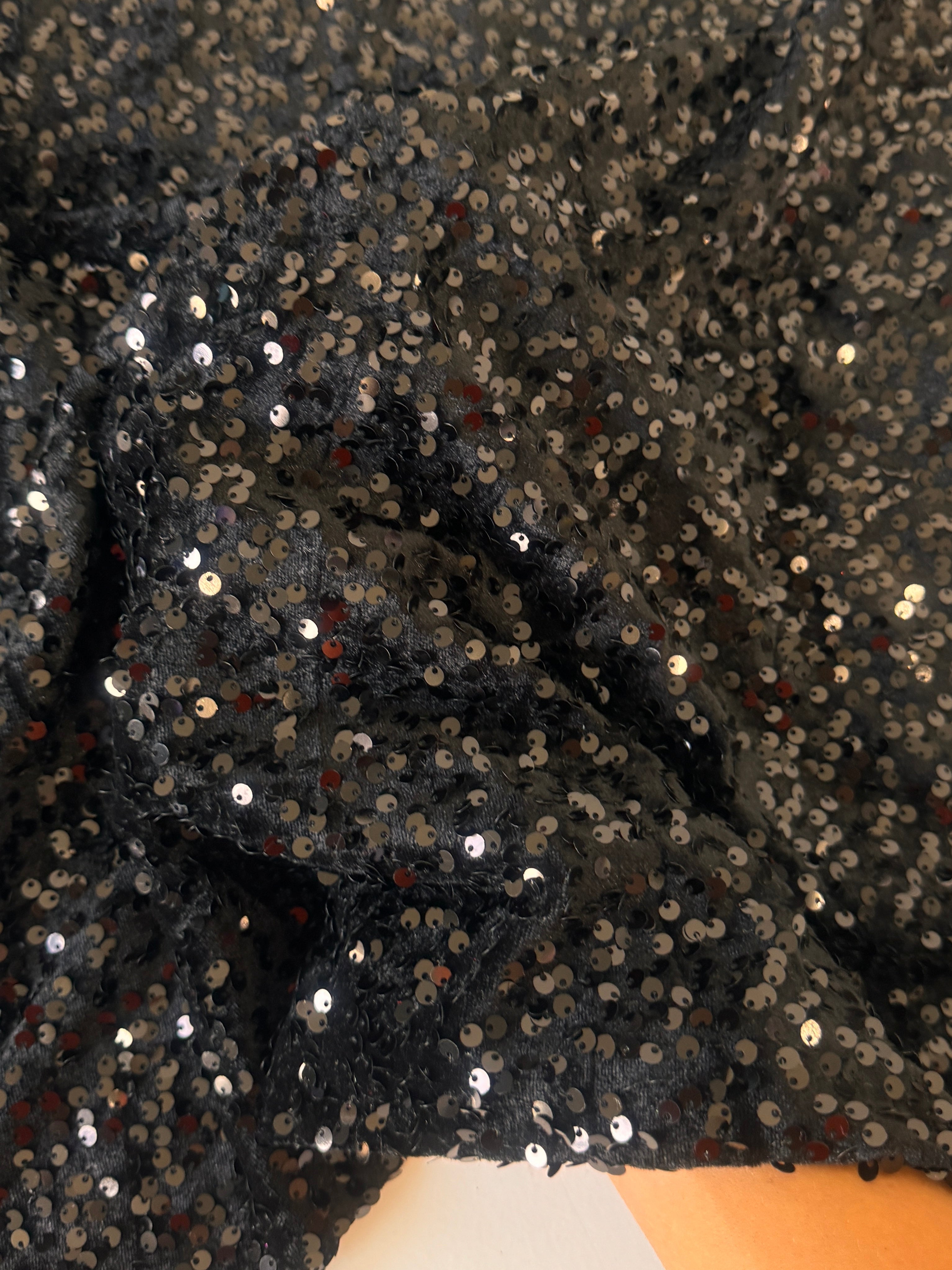 Black sequined fabric  showing shimmering silver and gold reflective sequins