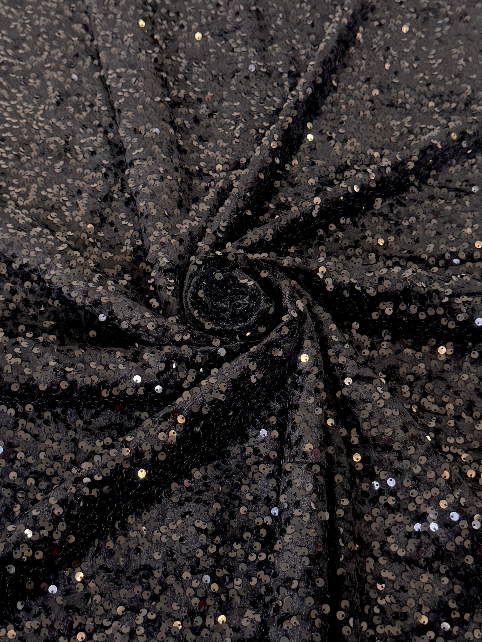 Black sequined fabric draped in a spiral pattern, showing shimmering silver reflection  