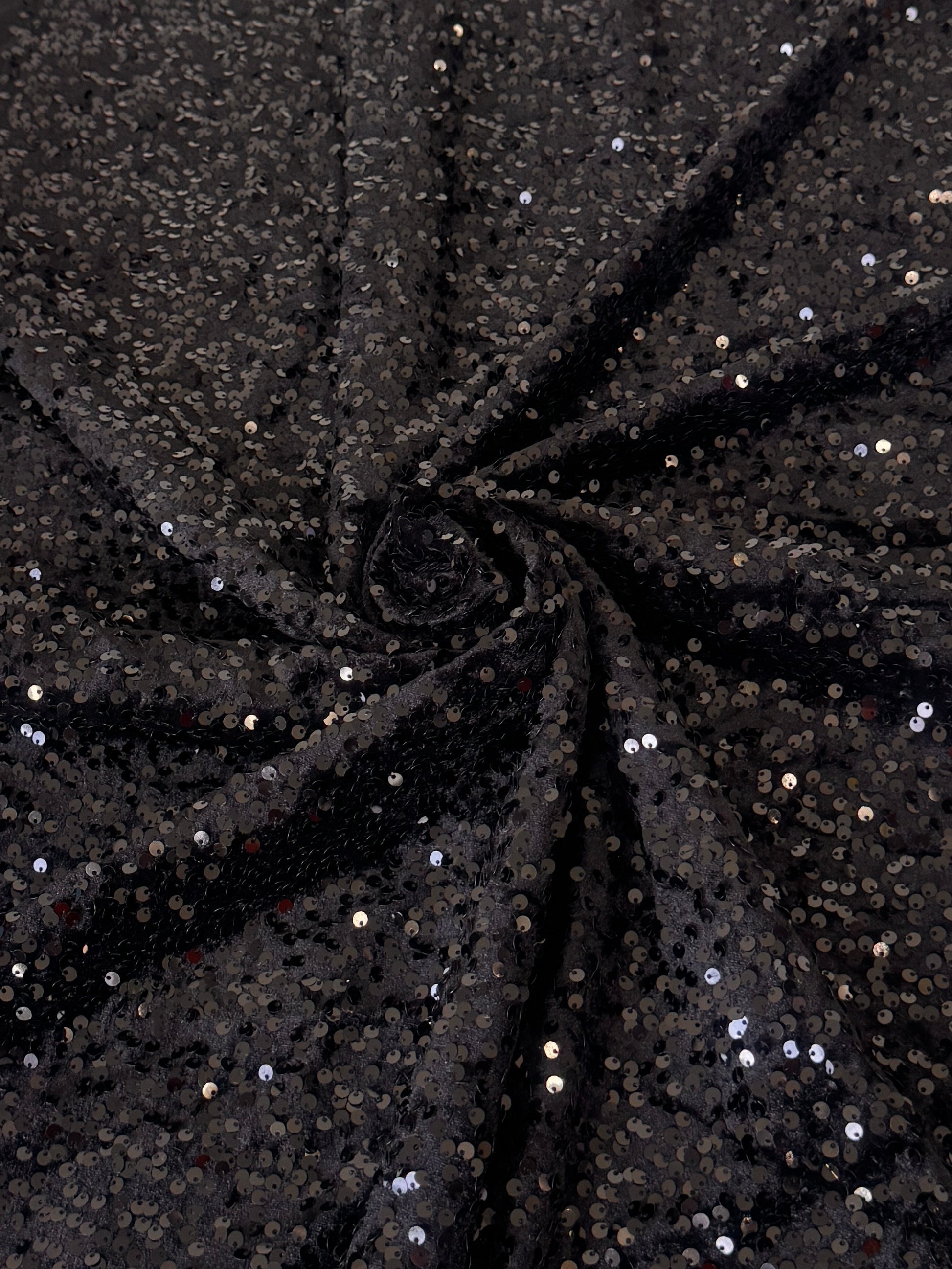 Black sequined fabric draped in a spiral pattern, showing shimmering silver and gold reflective sequins 