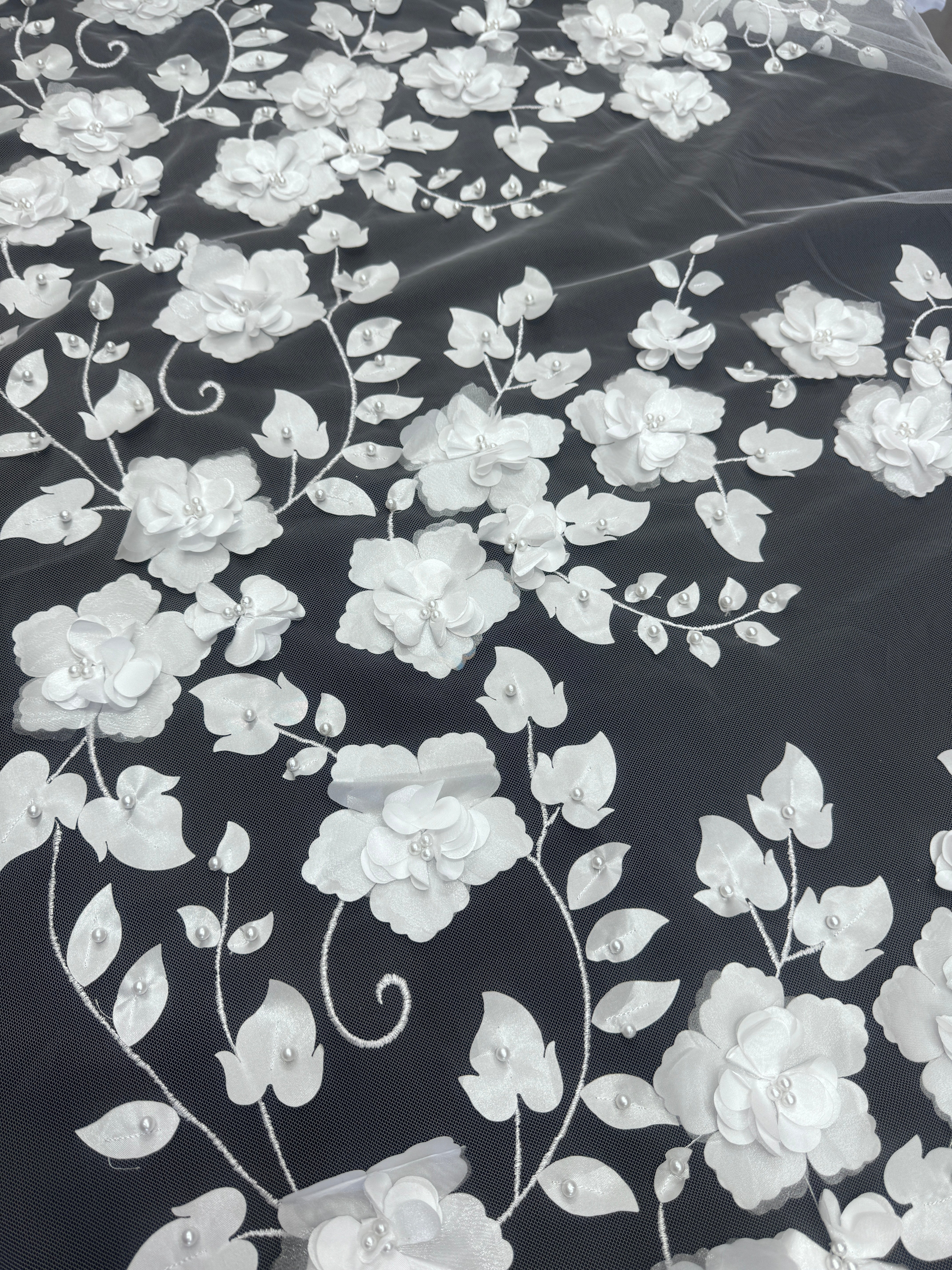 White floral embroidered fabric with 3D flower appliqués and pearl-like bead details on a black mesh background.