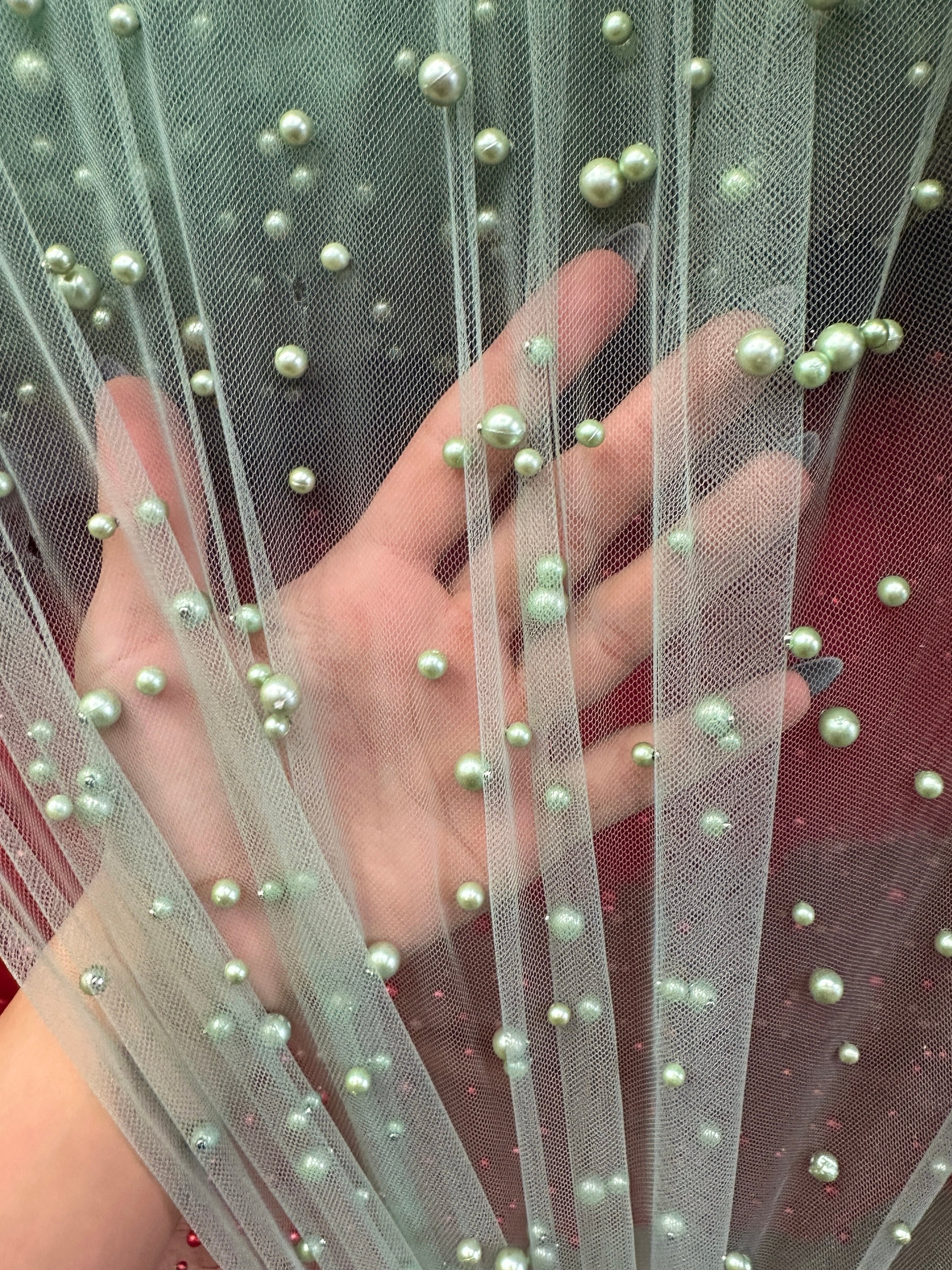 Close-up of a hand holding mesh  tulle fabric with pearl embellishments.