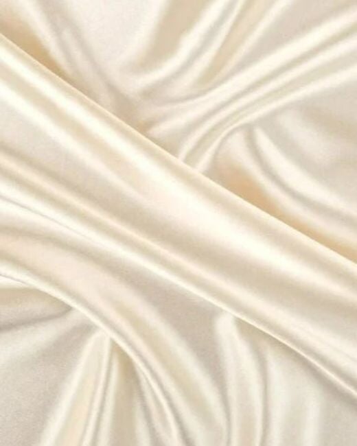 A close-up of draped silk satin fabric in a warm ivory or cream color, showing soft folds and a smooth, lustrous texture.