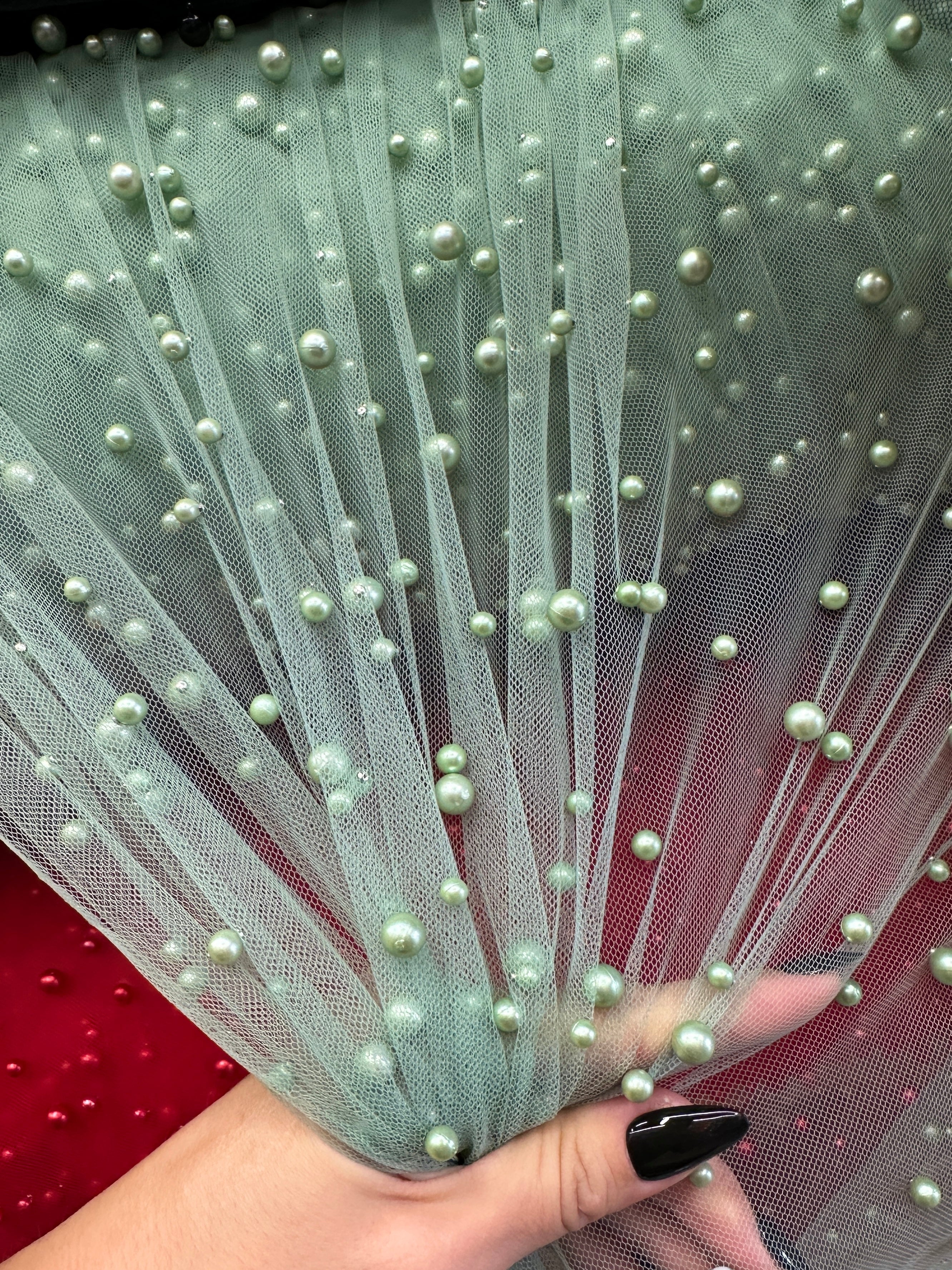 Sheer fabric with pearl embellishments held by a hand against a red background