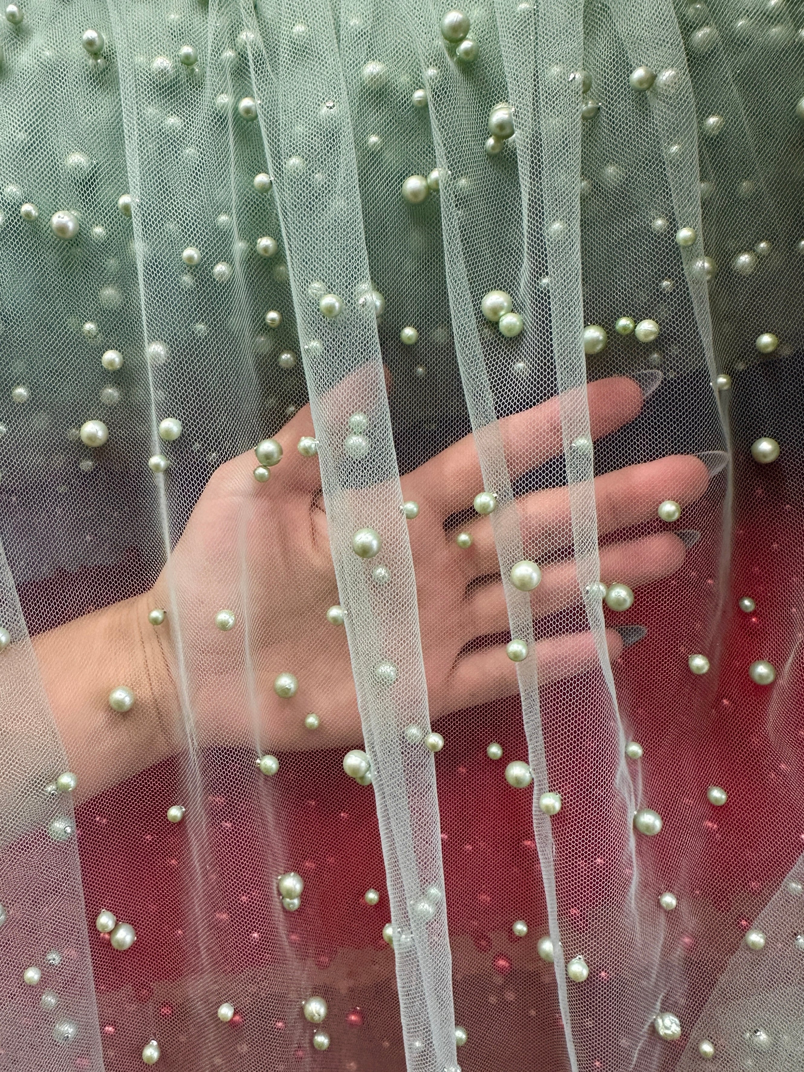 tulle fabric with embedded pearls held by a hand against a blurred background