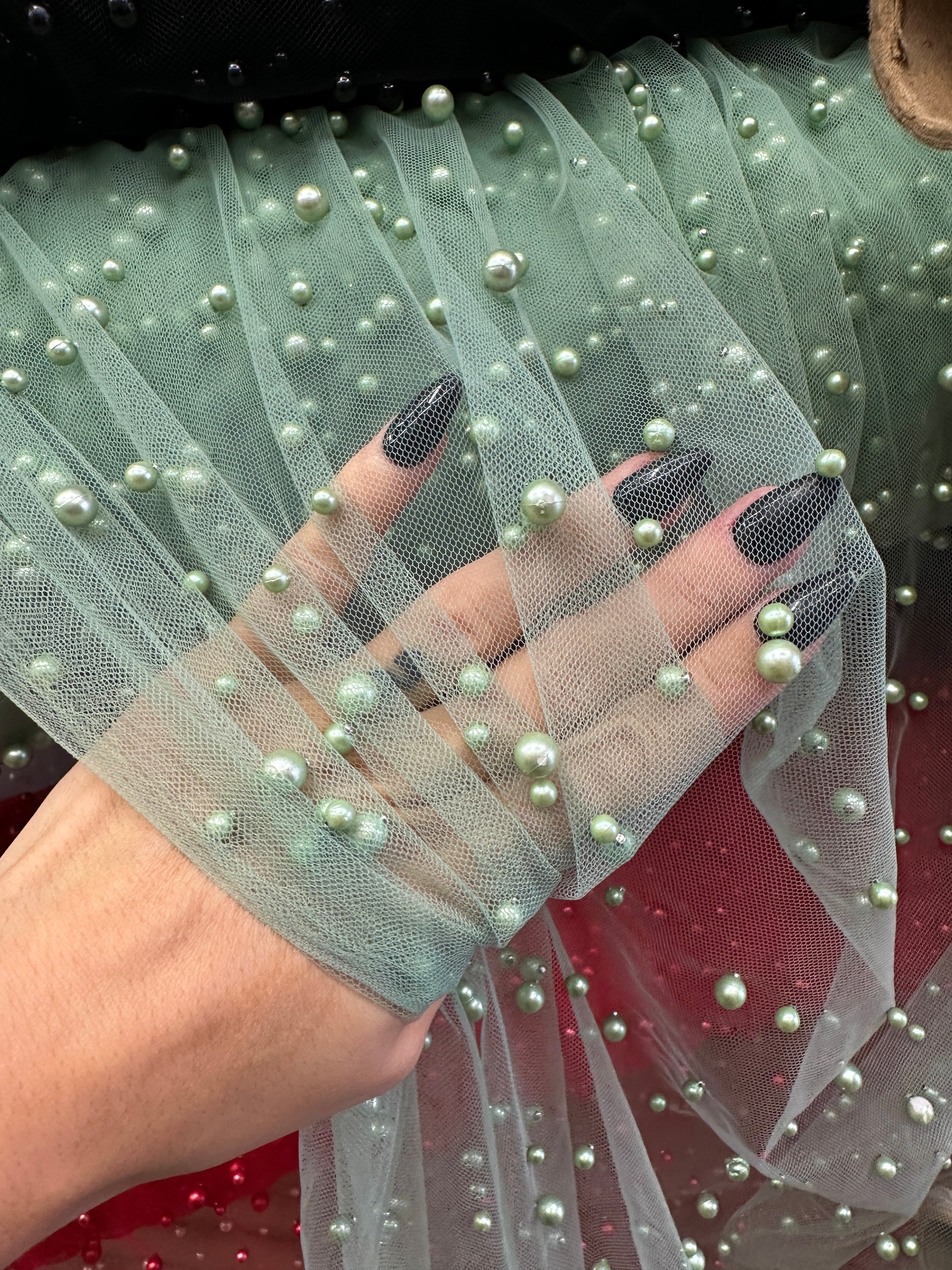 Hand wrapping a sheer green tulle fabric with pearl embellishments.