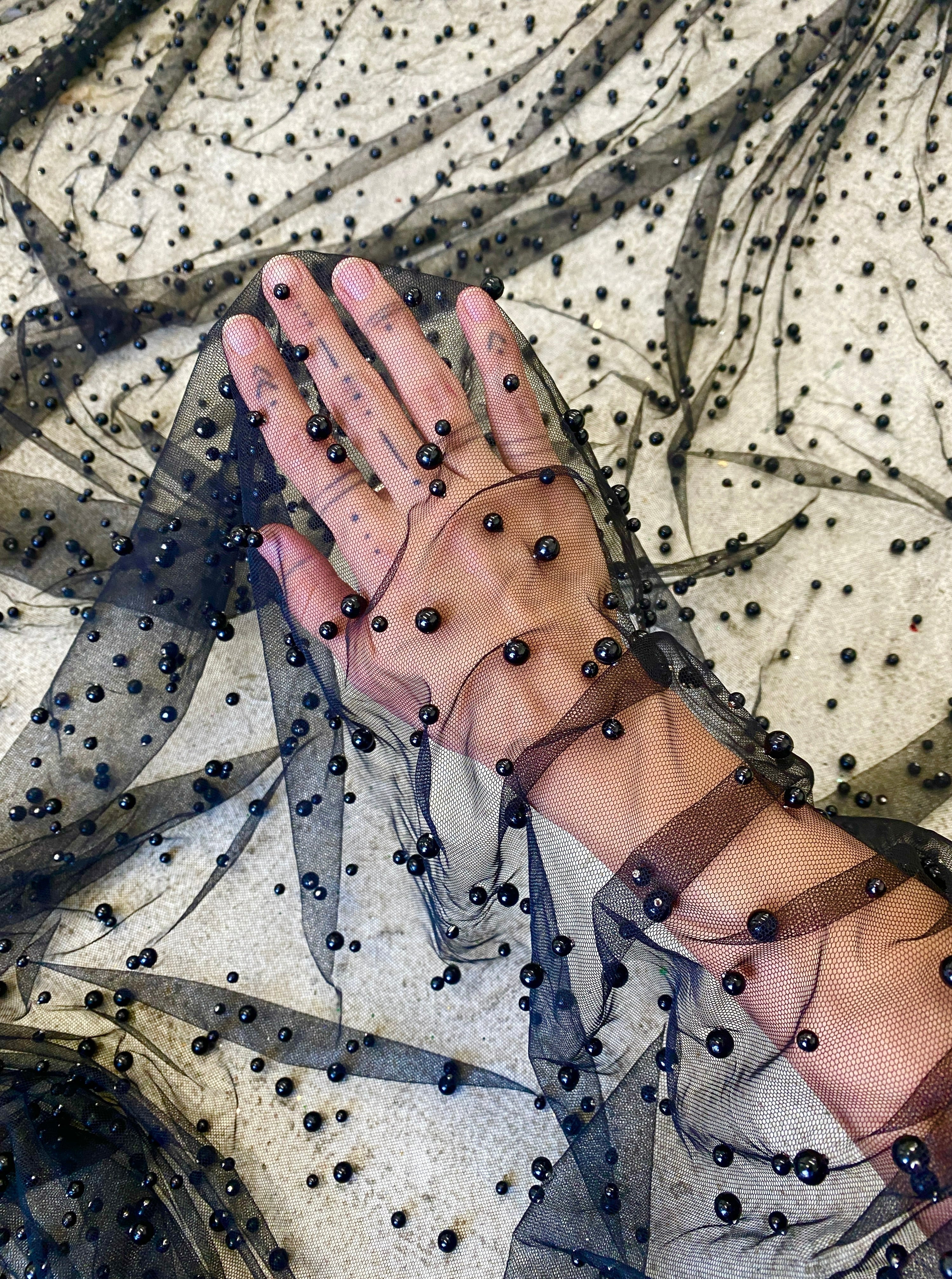 hand reaching through black beaded tulle fabric 