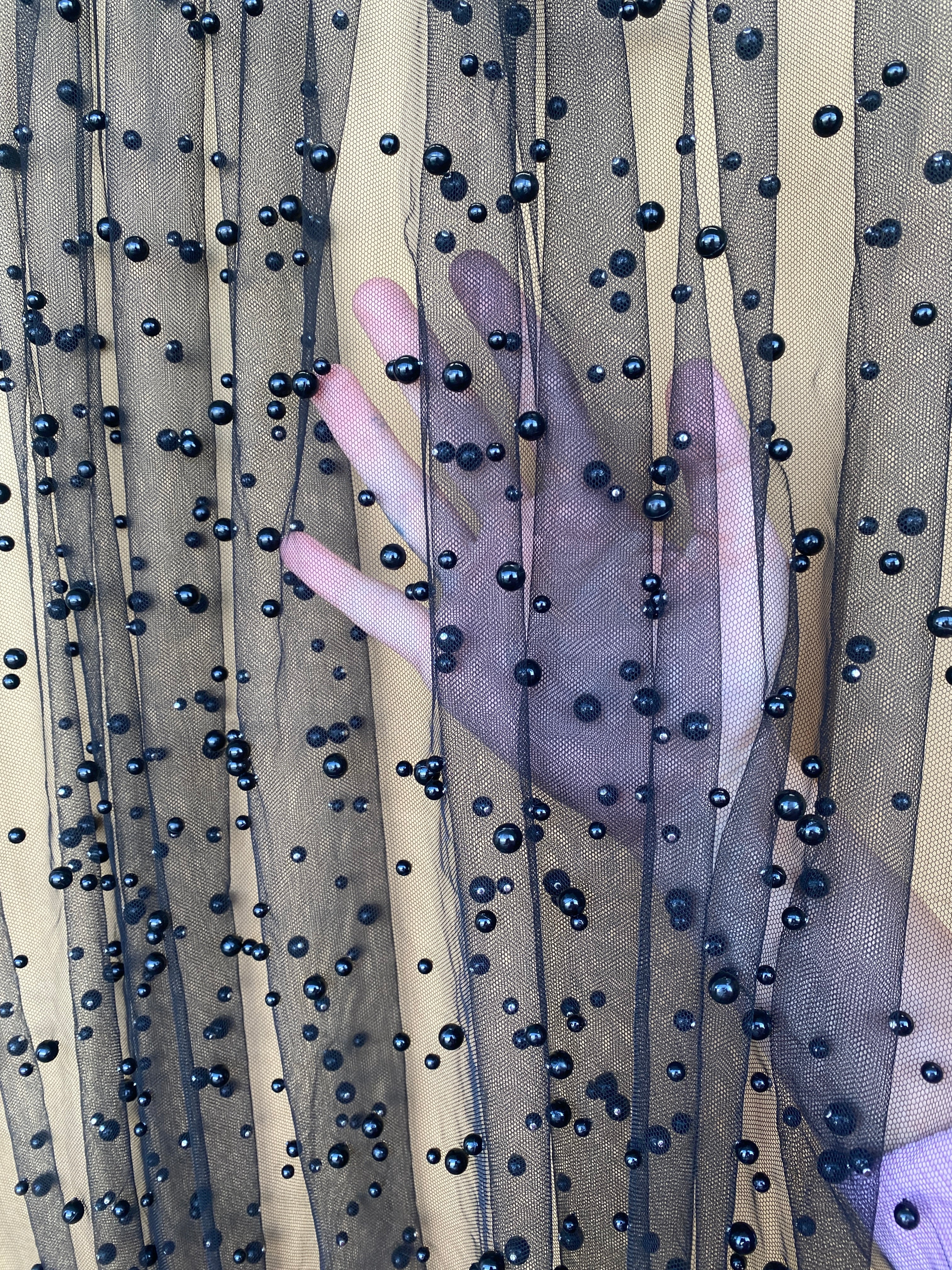 Hand reaching through a sheer fabric with black beads